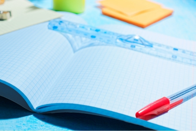 方眼ノートの上に定規と赤いボールペンが置かれた学習用デスクの写真