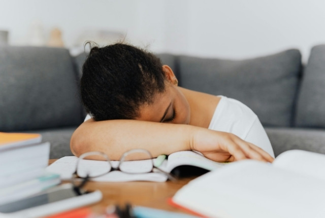 机に広げた教材の前で腕に顔を伏せて眠ってしまった学習中の人物