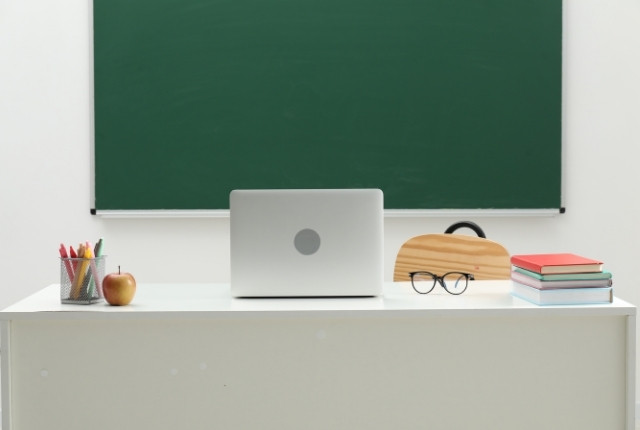 黒板の前の机にノートパソコンと文房具が置かれた教室風景