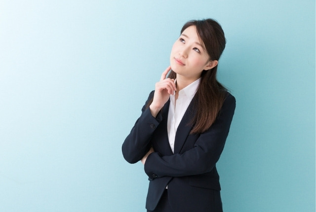 スーツ姿の女性が腕を組み、考え込むような表情で立っているビジネスイメージ写真