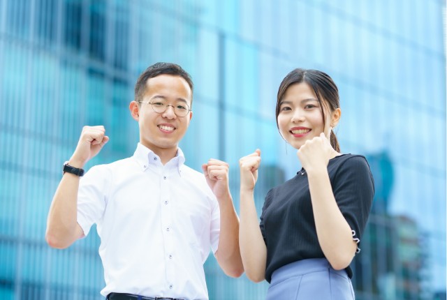 ビジネス街を背景に笑顔でガッツポーズをする男女の様子