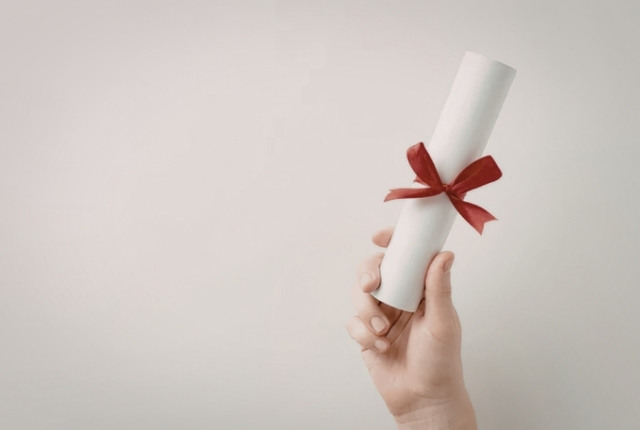 赤いリボンが付いた丸めた証書を手で持っている様子