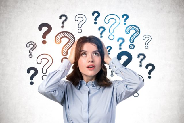 外国人に漢字学習が難しい理由 の周りに複数の疑問符が浮かび、困った表情で考え込む女性のイメージ写真