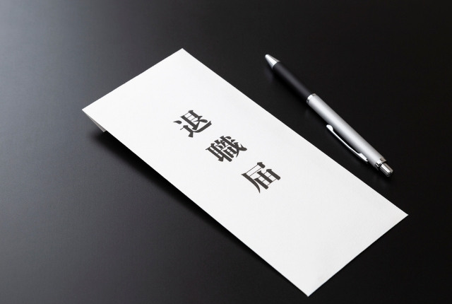 退職届と書かれた書類とボールペンが黒い机の上に置かれている様子